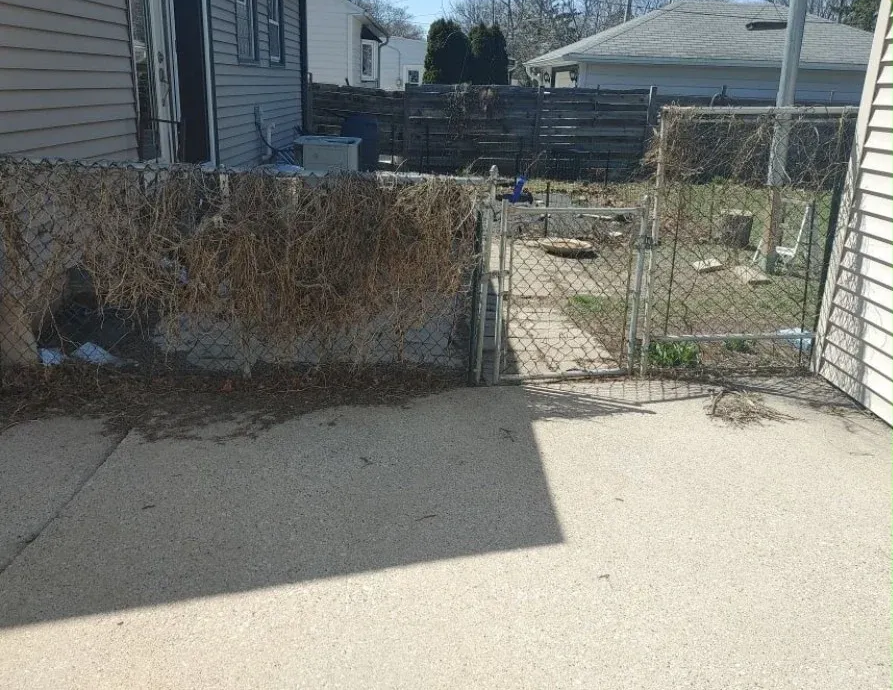 Backyard with concrete patio, chain-link gate, and fenced garden area under bright sunlight
