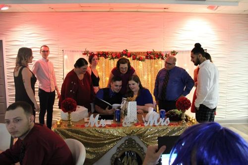 Wedding ceremony with couple signing a document at a decorated table, surrounded by guests in a festive room.