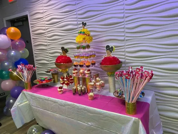 Party table with treats, balloons, and Mickey Mouse decorations in front of a textured wall.