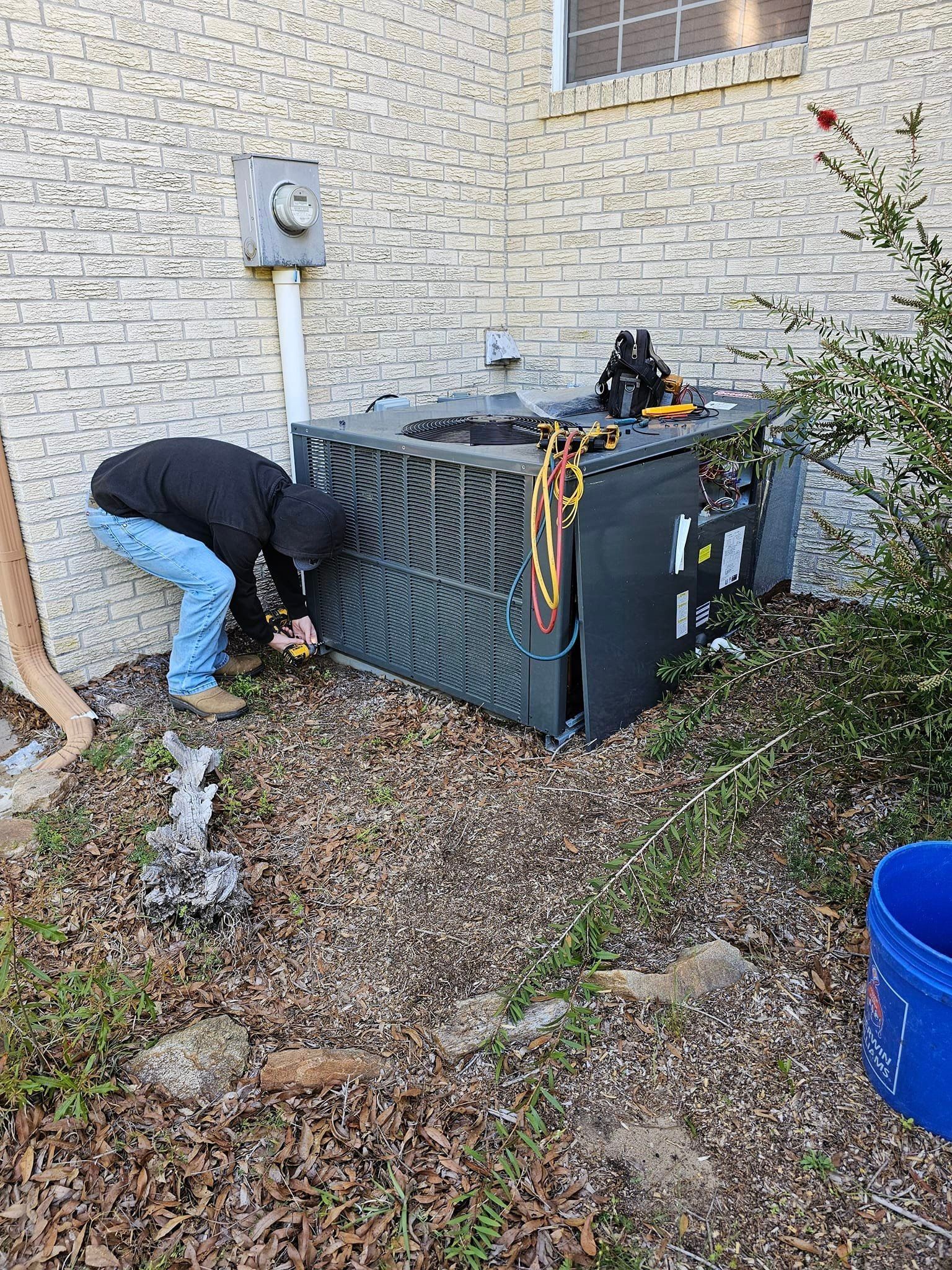 A man is working on an air conditioner outside of a house.