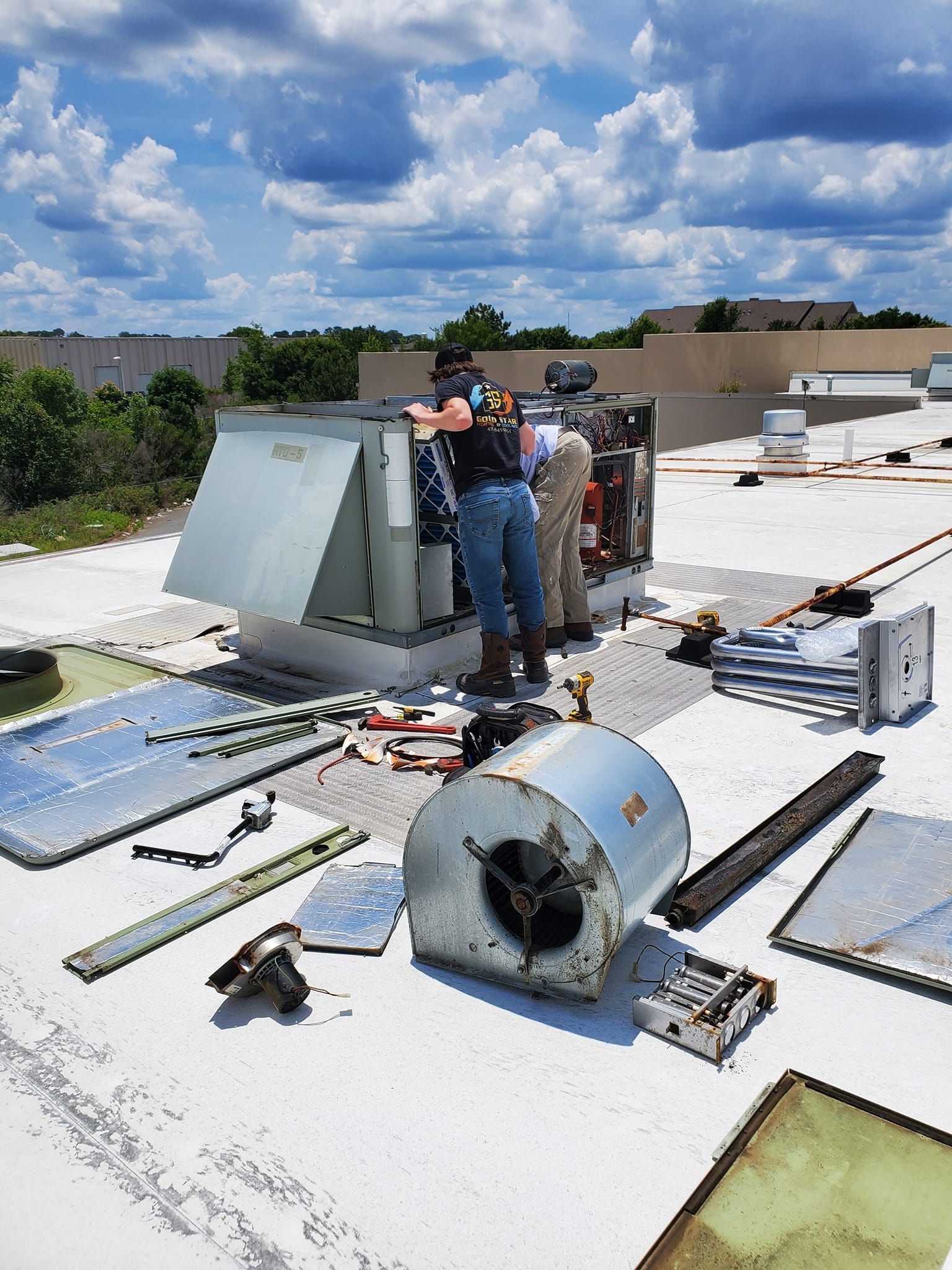 A group of men are working on an air conditioner on the roof of a building.