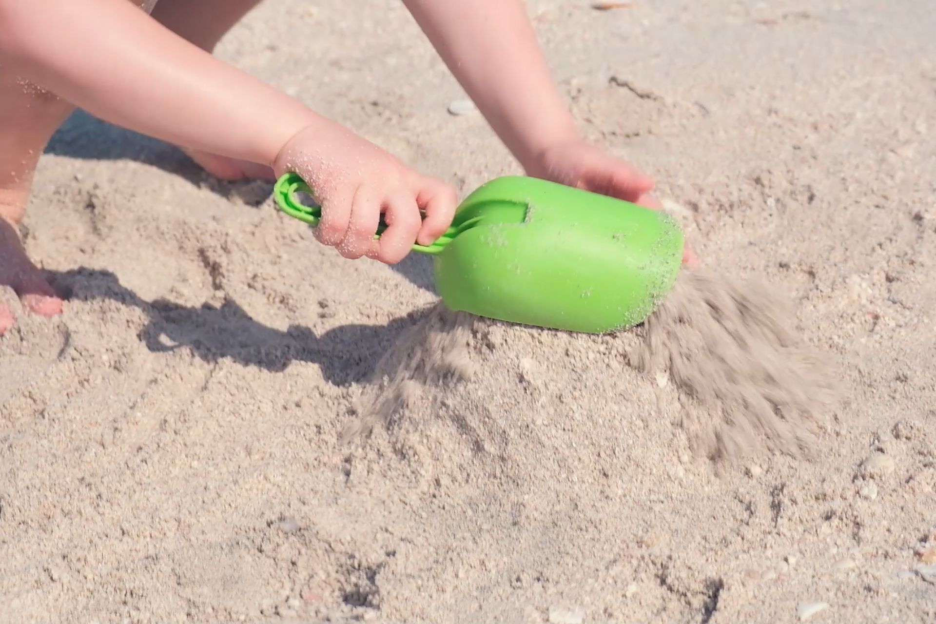 Child's hands playing with green sand shovel in the sand at the beach.