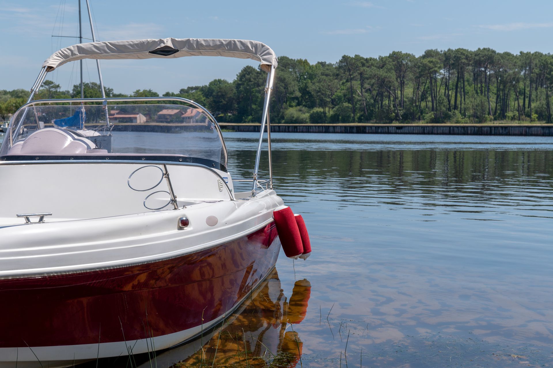 White and red boat floating on calm water near a treeline.