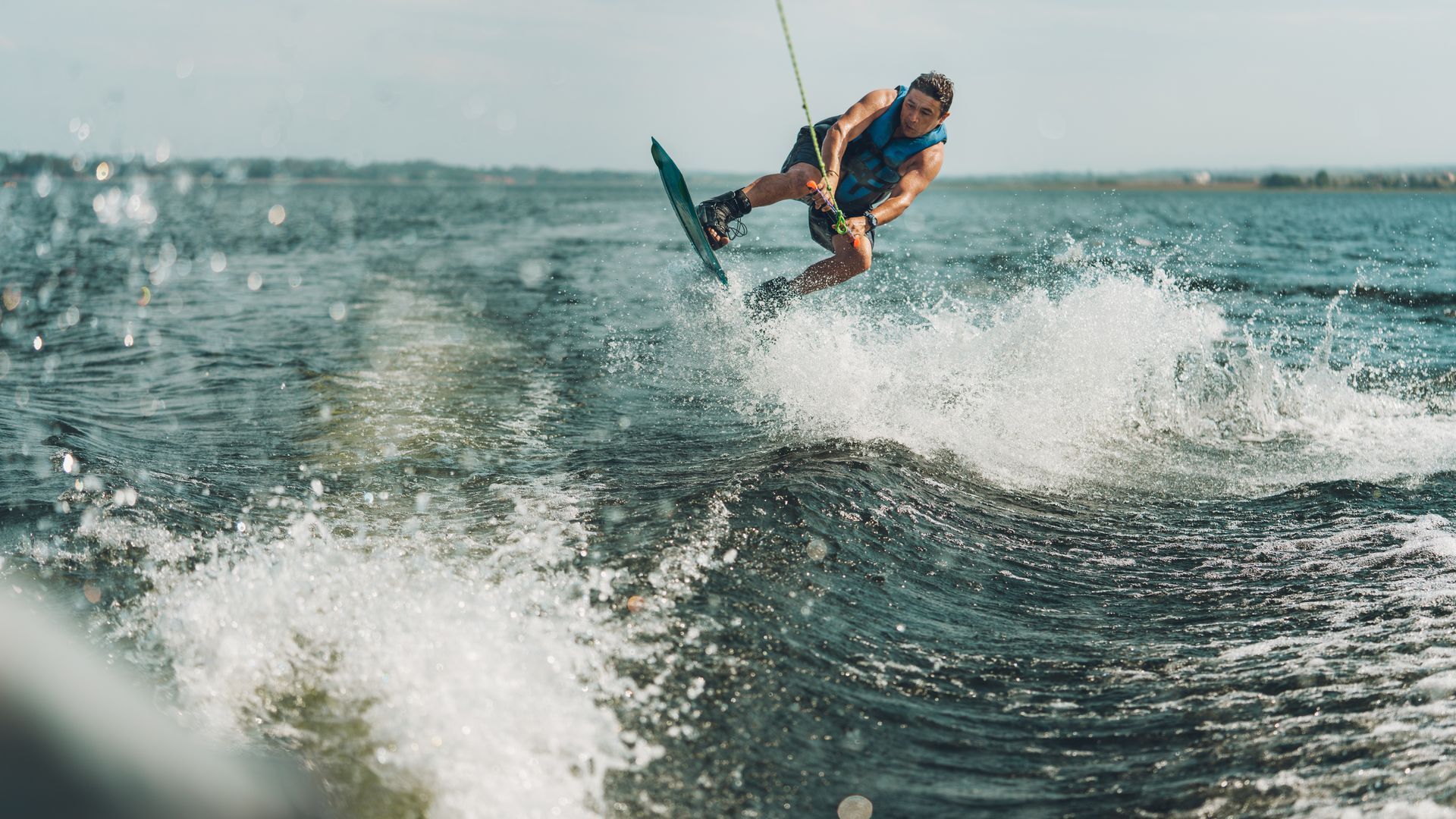 Wakeboarder in mid-air above water, blue board, sunny day.