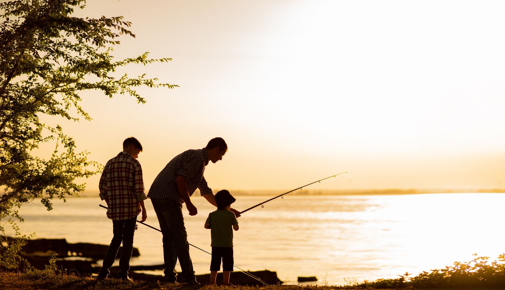Father and two sons fishing on a lake at sunset.
