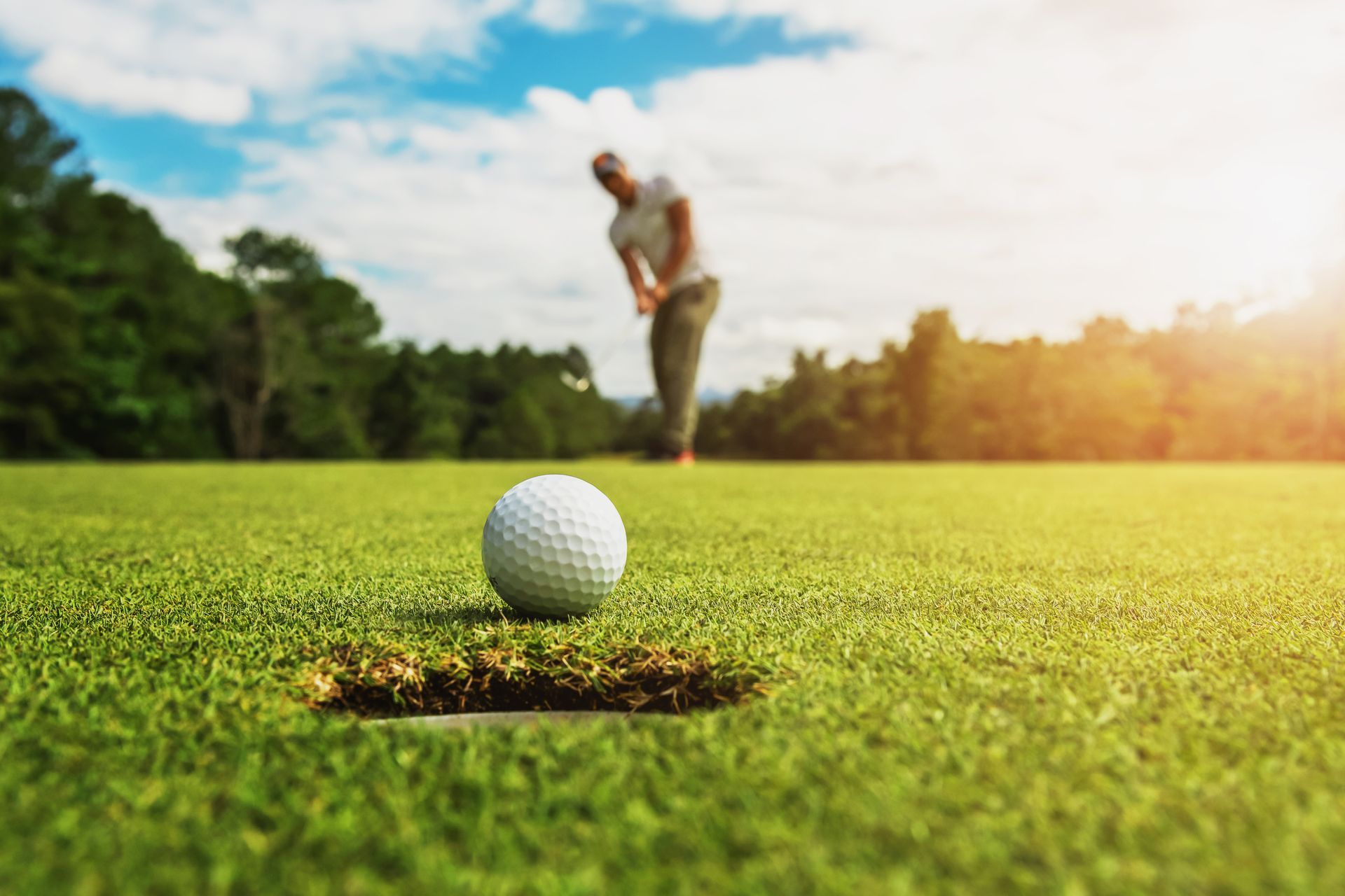 A golfer about to putt a white golf ball into the hole on a green, sunny golf course.