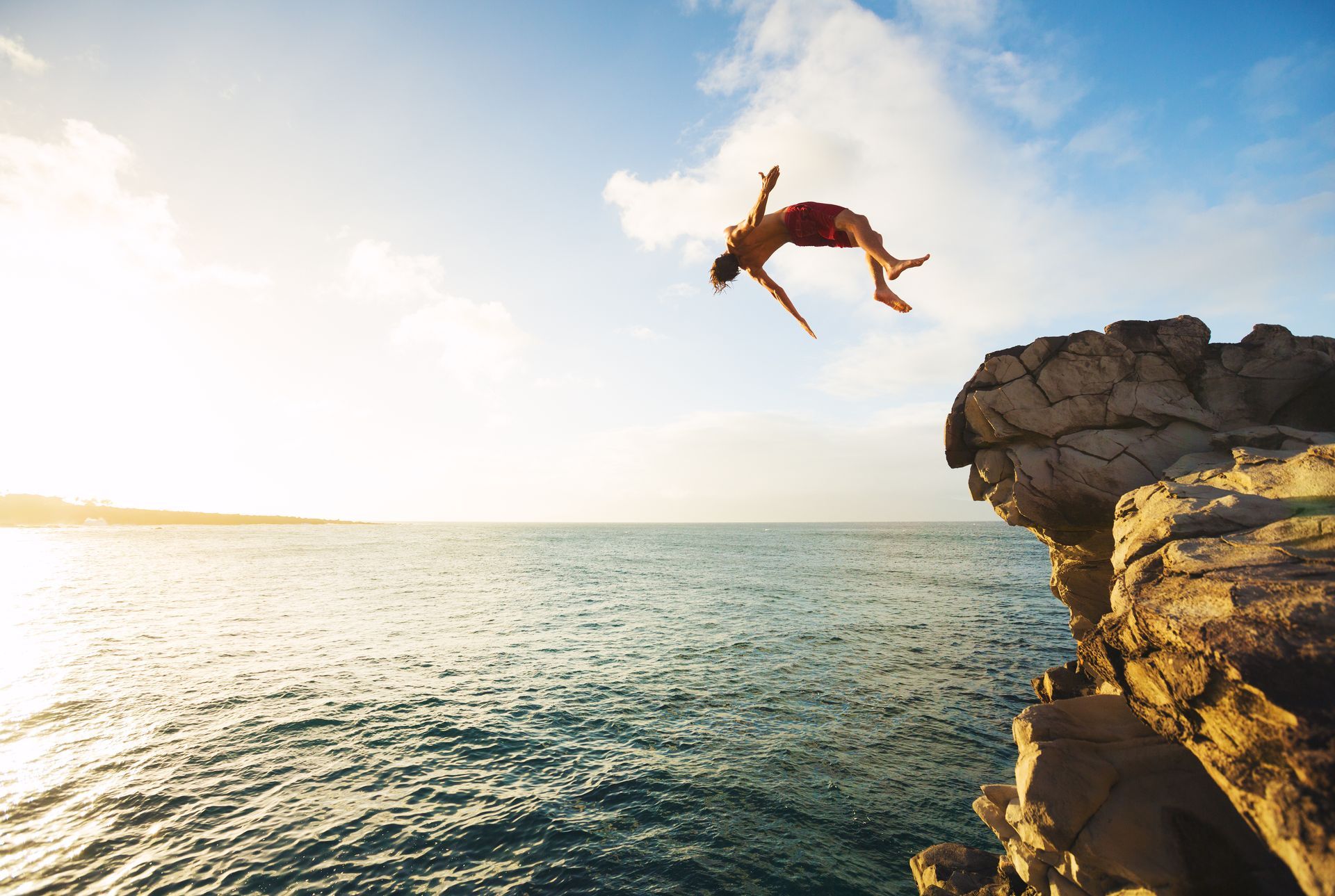A man is jumping off a cliff into the ocean.