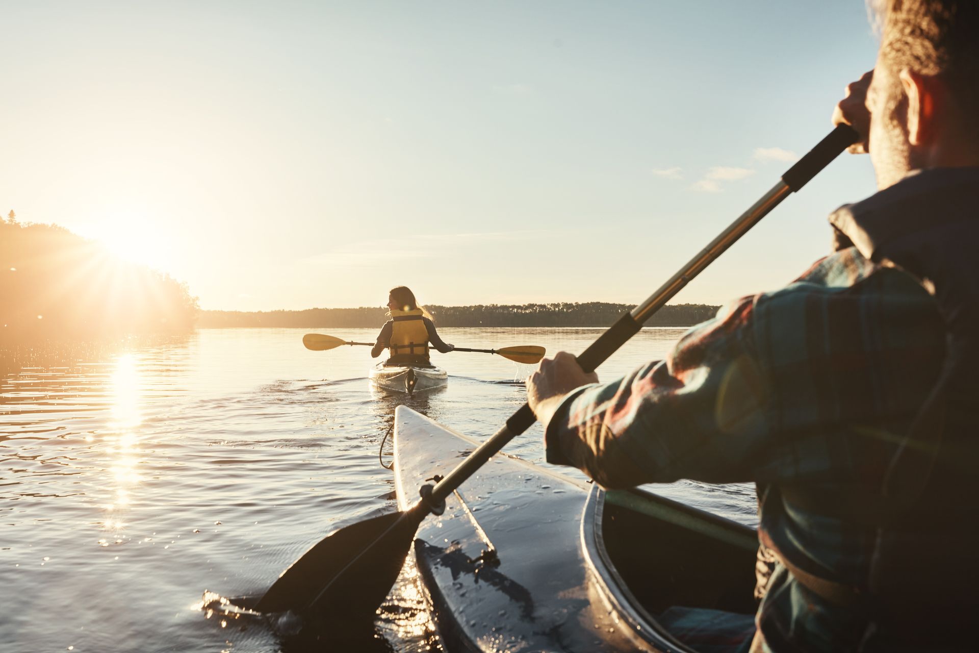 Two people kayaking on a lake at sunset; one in the foreground, one in the distance.
