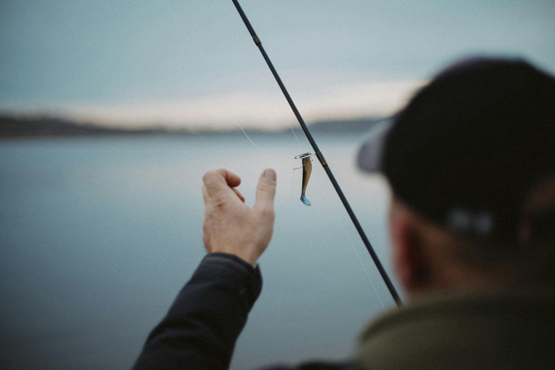 A man is holding a small fish on a fishing rod.