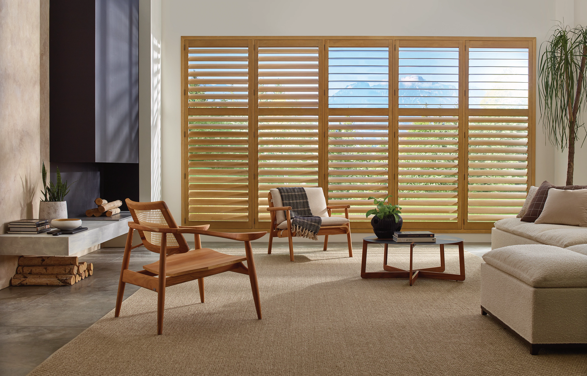 Modern living room with wooden chairs, beige sofa, coffee table, fireplace, and large window blinds
