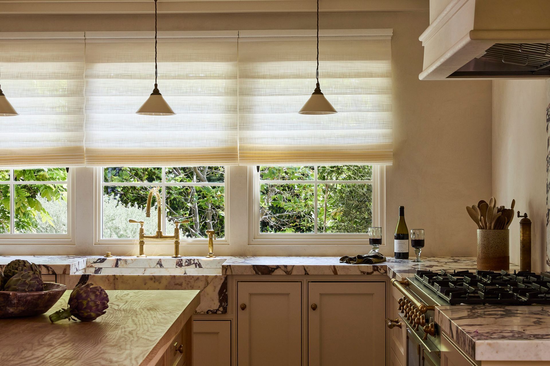 Bright kitchen with large windows, beige blinds, marble counters, and a gas stove with utensils.