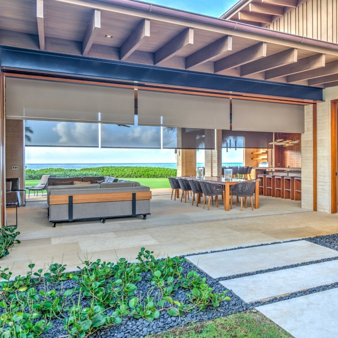 Covered outdoor patio with dining table, grill, and rolling glass doors overlooking a green landscape