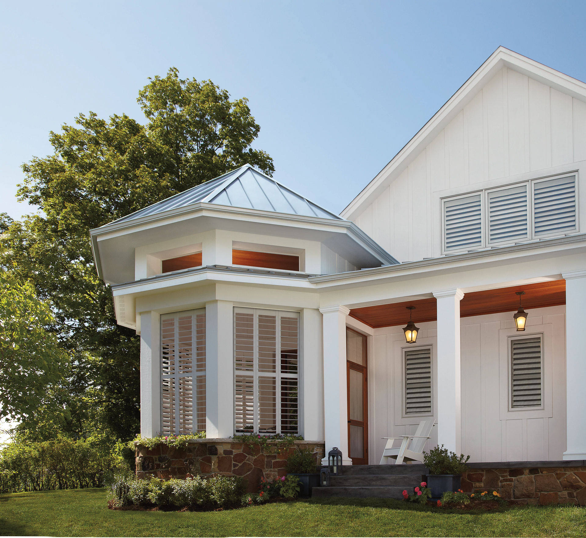 White farmhouse with porch and metal roof in sunny yard with trees and blue sky