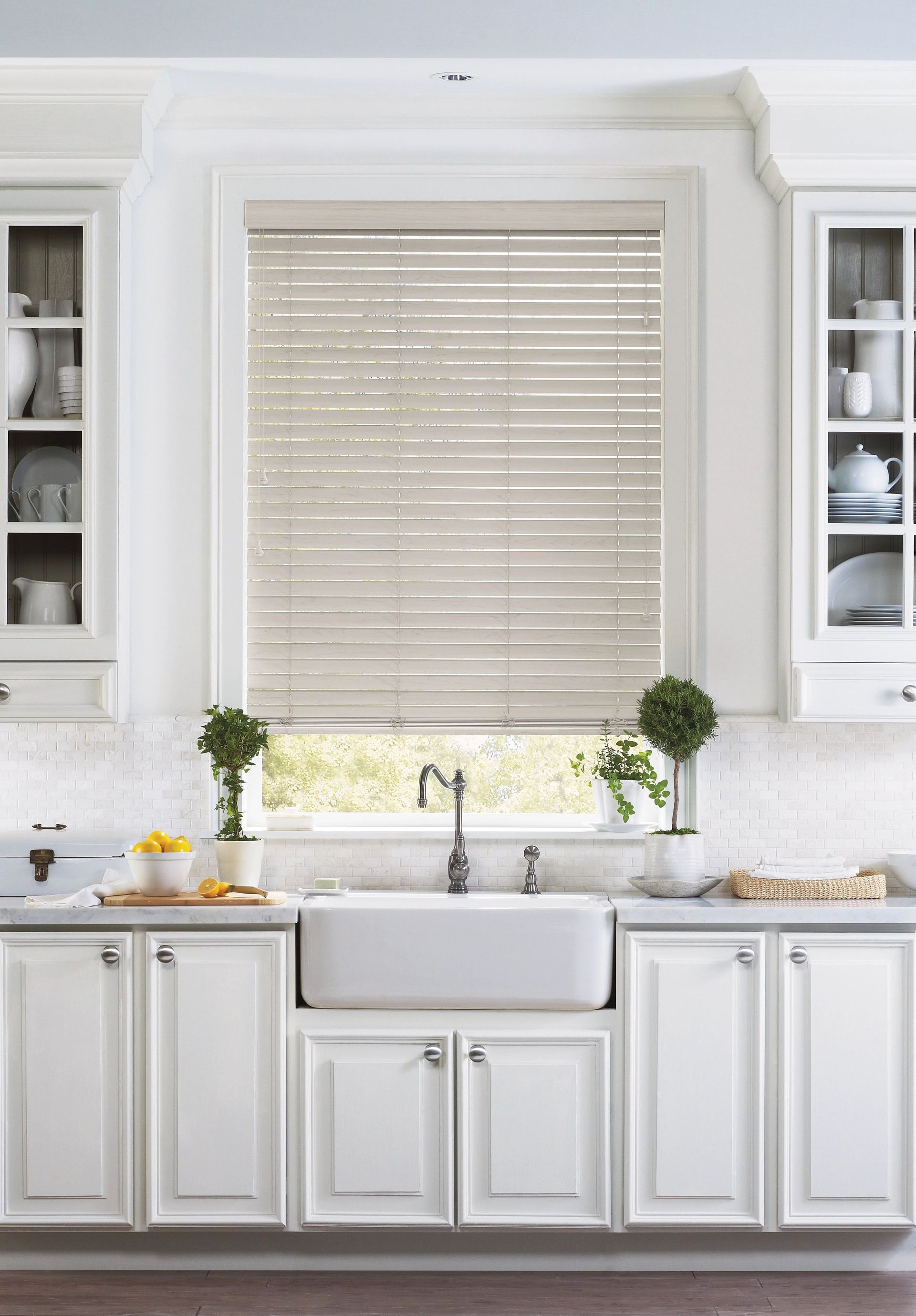 Bright white kitchen with farmhouse sink beneath a window and beige blinds, flanked by built-in shelves.