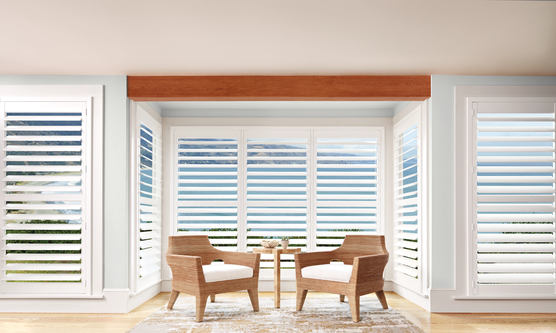 Bright sunroom with white shutters, a central window seat, and two wicker chairs facing a small table.