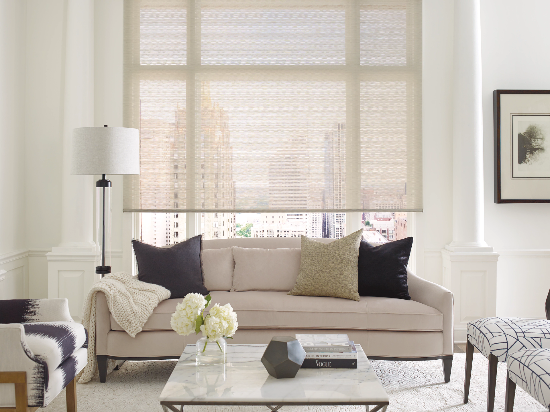 Bright living room with beige sofa, patterned armchairs, floor lamp, and large window blinds