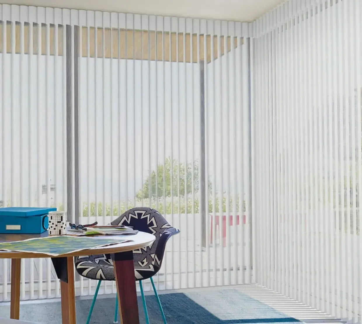 Bright living room with sheer curtains, a blue rug, and a wooden table with chairs by a window.