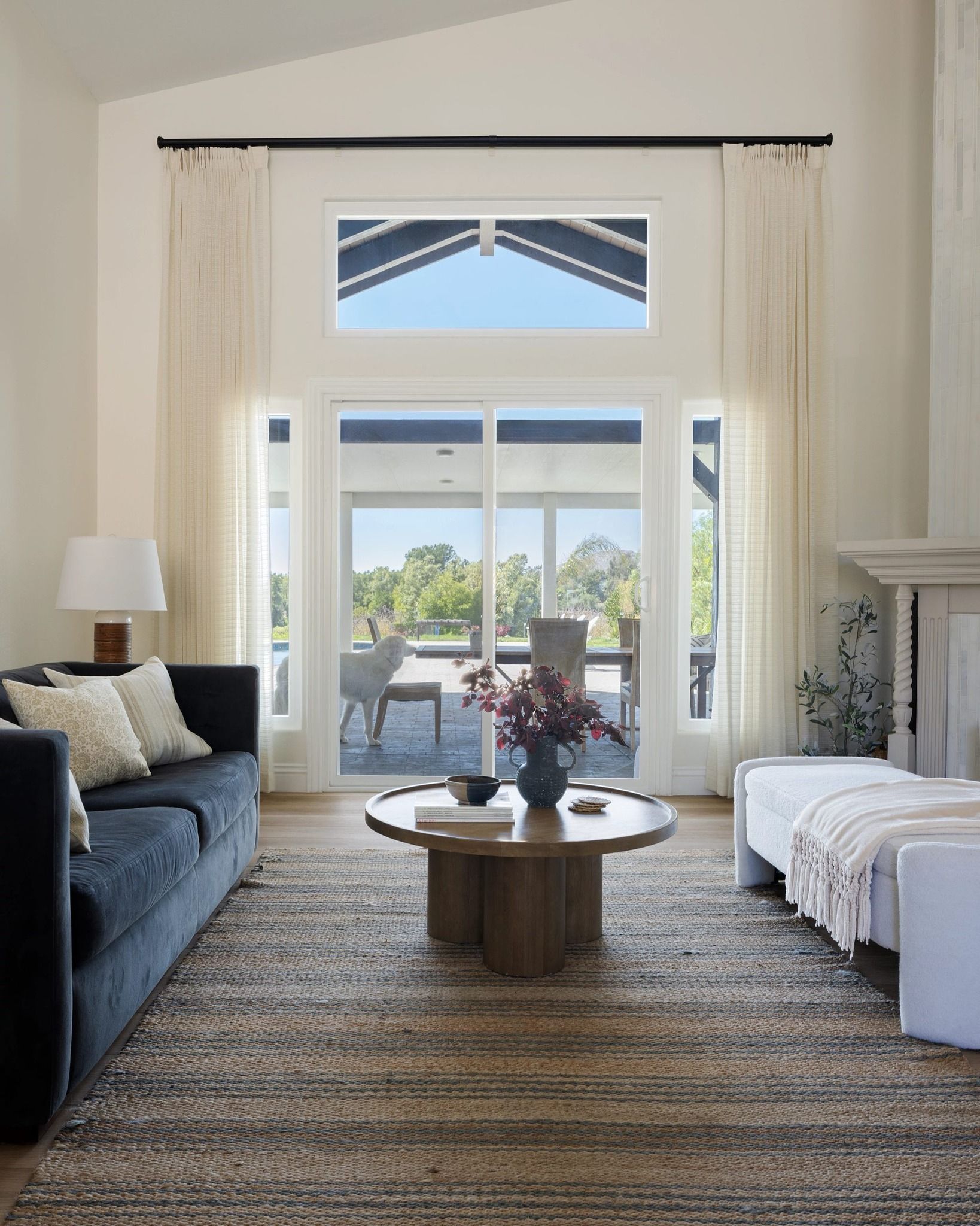 Bright living room with blue sofa, white chaise, round coffee table, and large French doors to a sunny patio