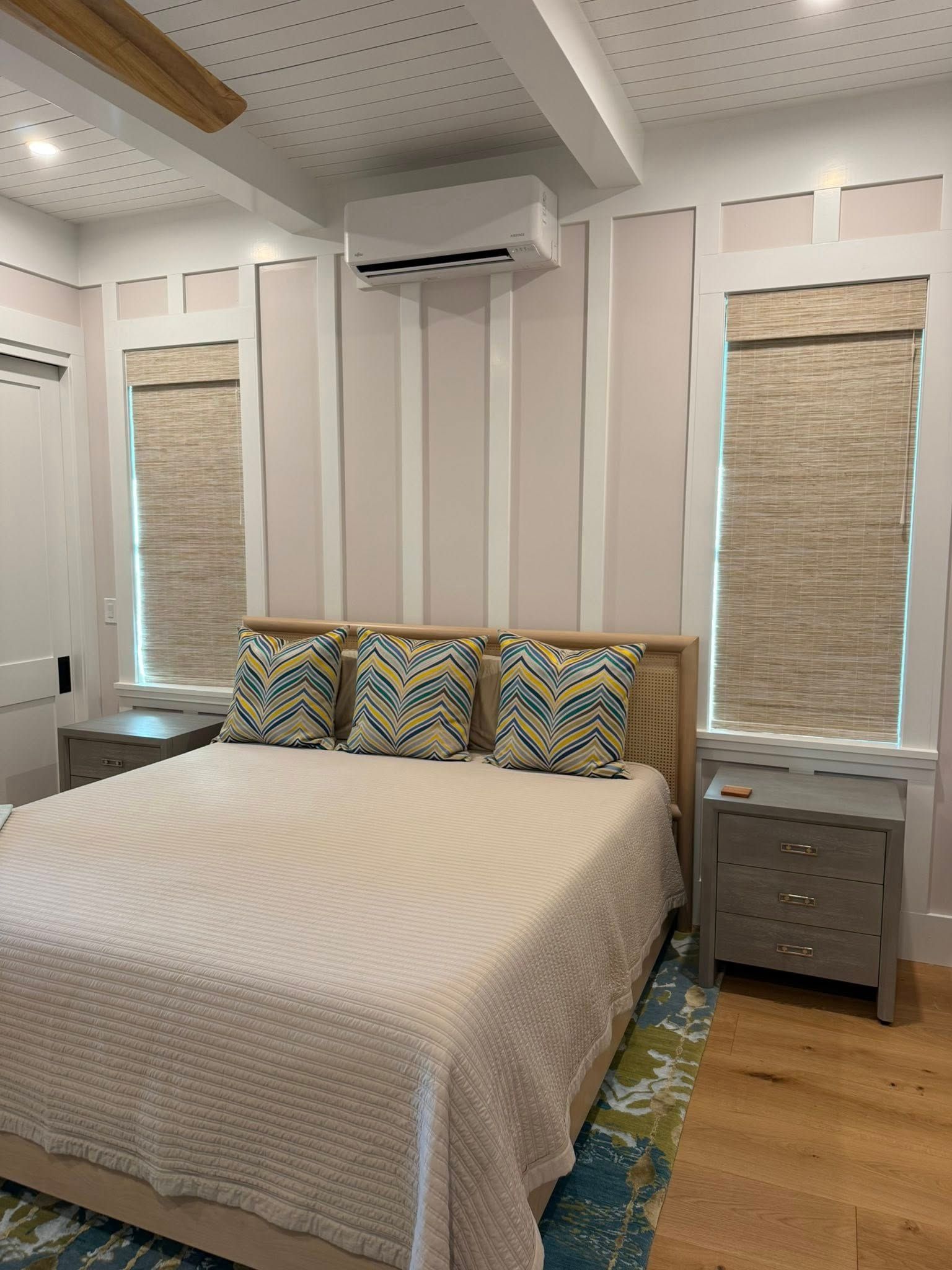 Bedroom with striped accent wall, bed, nightstand, and two windows with woven blinds
