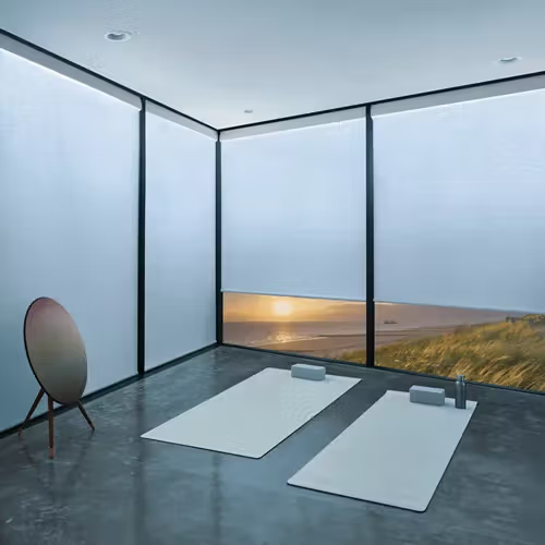 Minimalist modern yoga room with mats by a floor-to-ceiling window overlooking a grassy landscape
