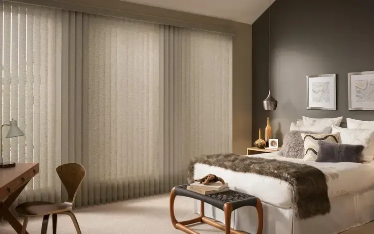 Modern bedroom with a king bed, floor-to-ceiling curtains, desk, chair, and warm neutral decor.