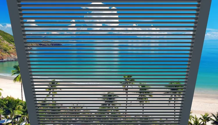 Tropical beach and turquoise ocean seen through horizontal window blinds, with palm trees below.