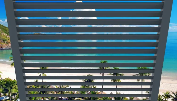 Horizontal gray slats frame a view of a turquoise pool and ocean beach beyond.