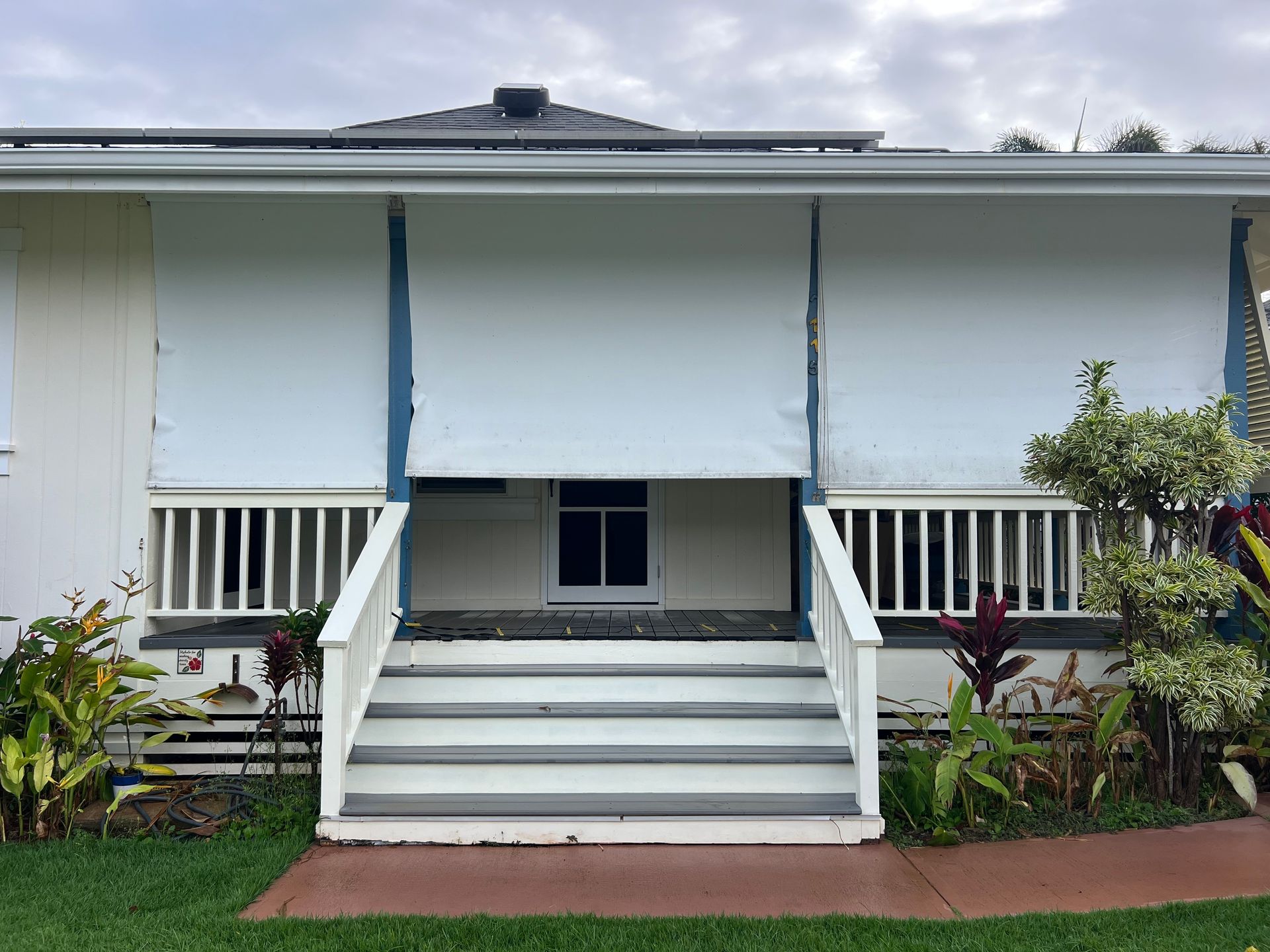 Front entrance of a white house with stairs, railings, and a small porch garden