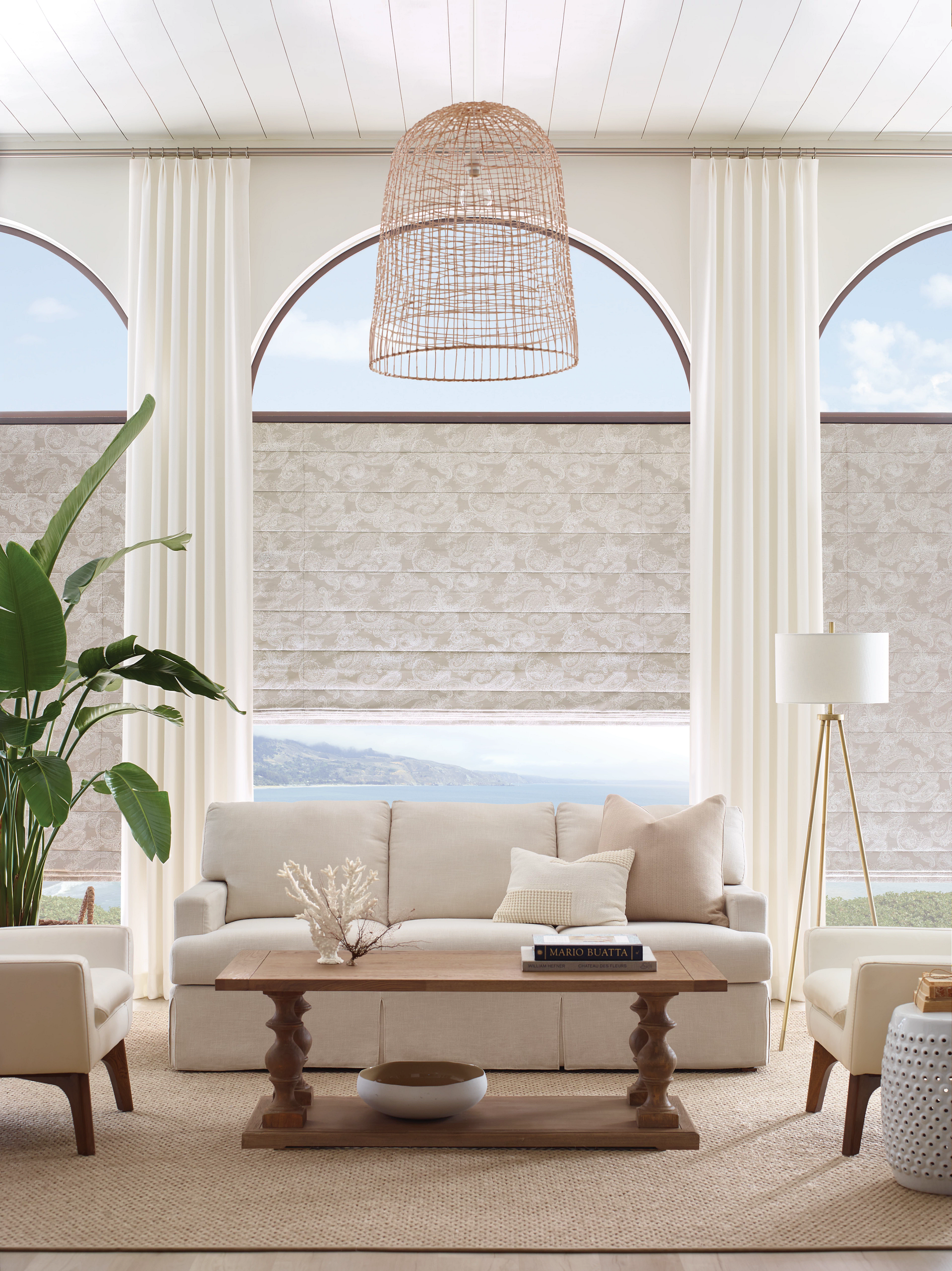Bright living room with arched windows, cream sofa, wooden coffee table, and woven pendant light