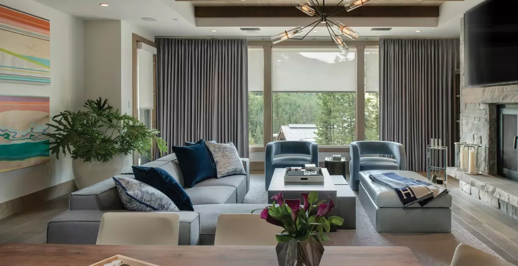 Bright living room with gray sofa, glass coffee table, large windows, and balcony chairs overlooking greenery