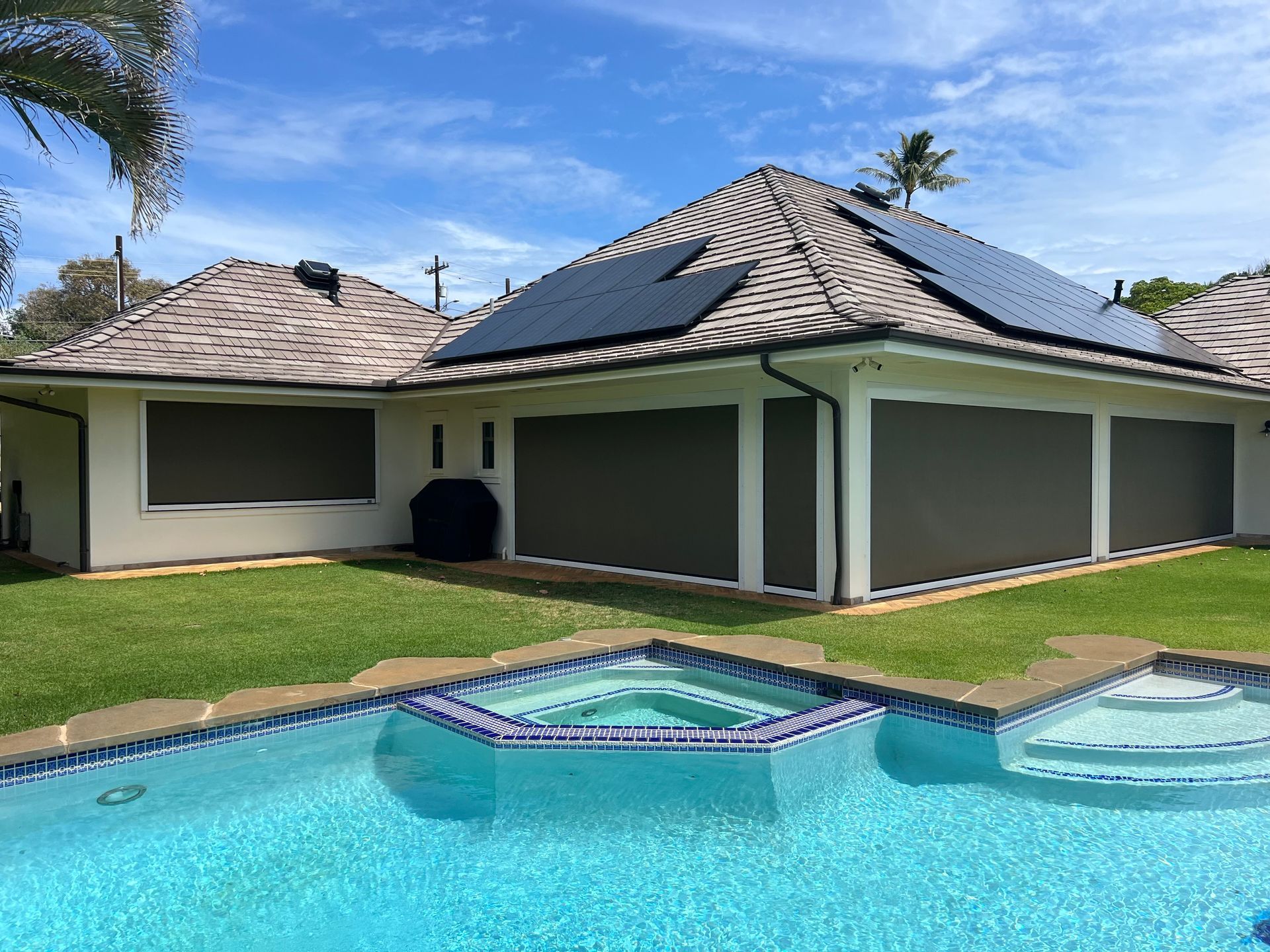 Modern house with tiled roof and screened patio beside a turquoise pool under a blue sky