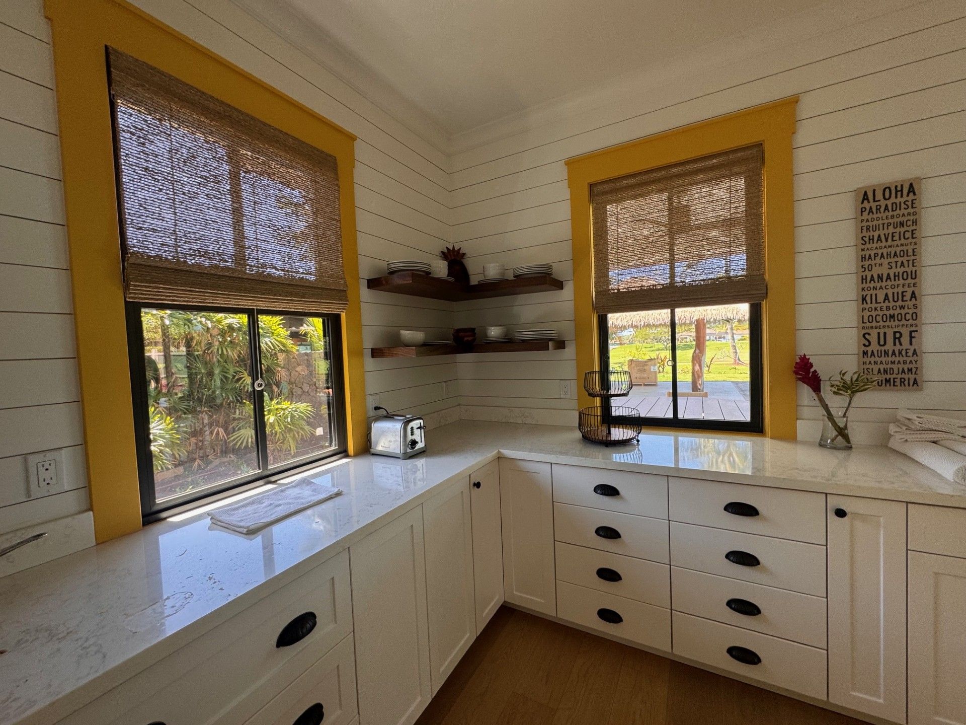 Bright kitchen with white counters, yellow-trimmed windows, open shelves, and black drawer pulls