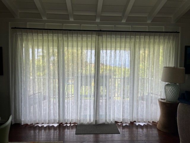 Sheer curtains over a large window in a living room, with a small table lamp on the right