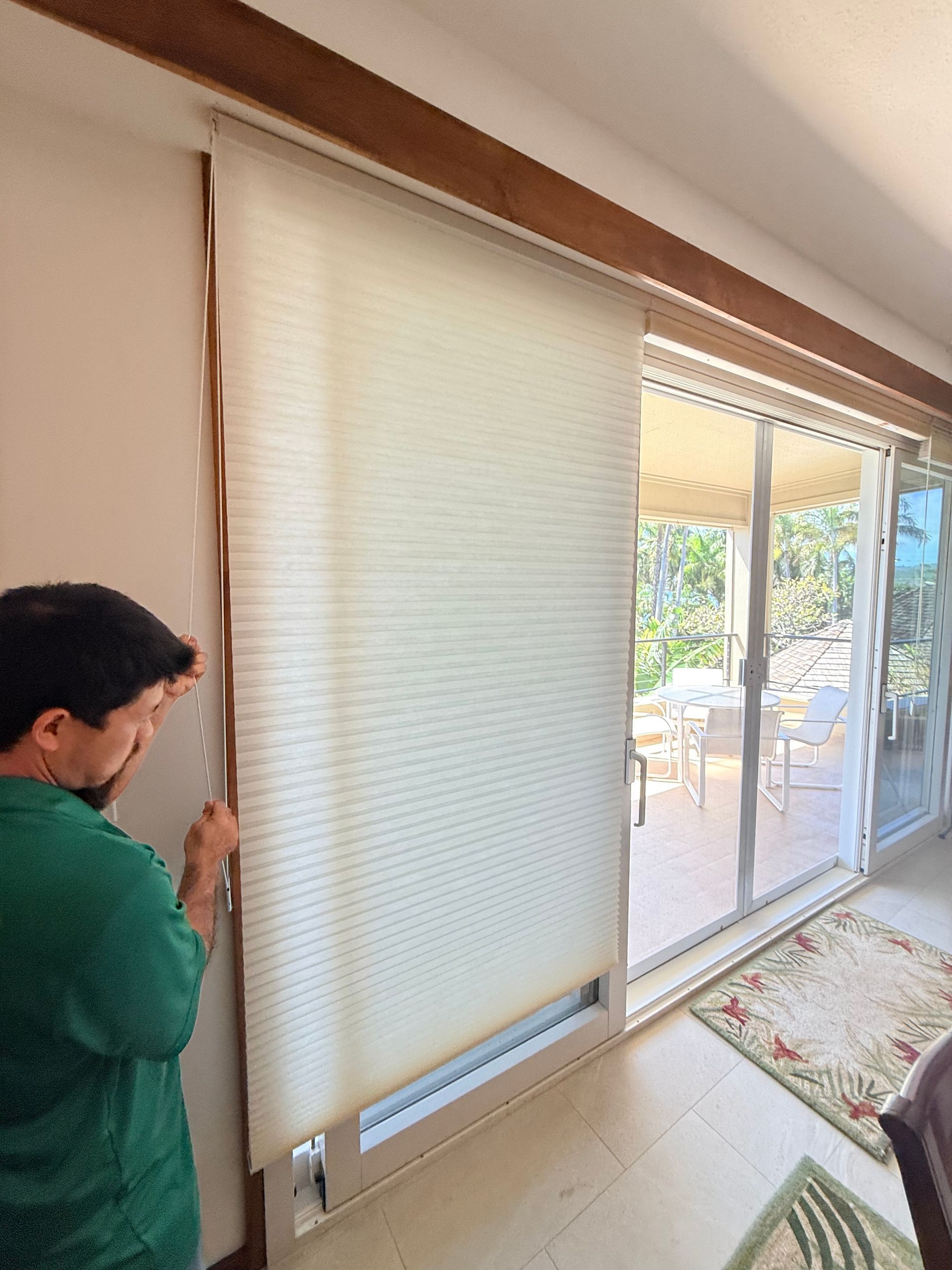 Person adjusting a white window blind beside a sliding glass door in a sunlit room