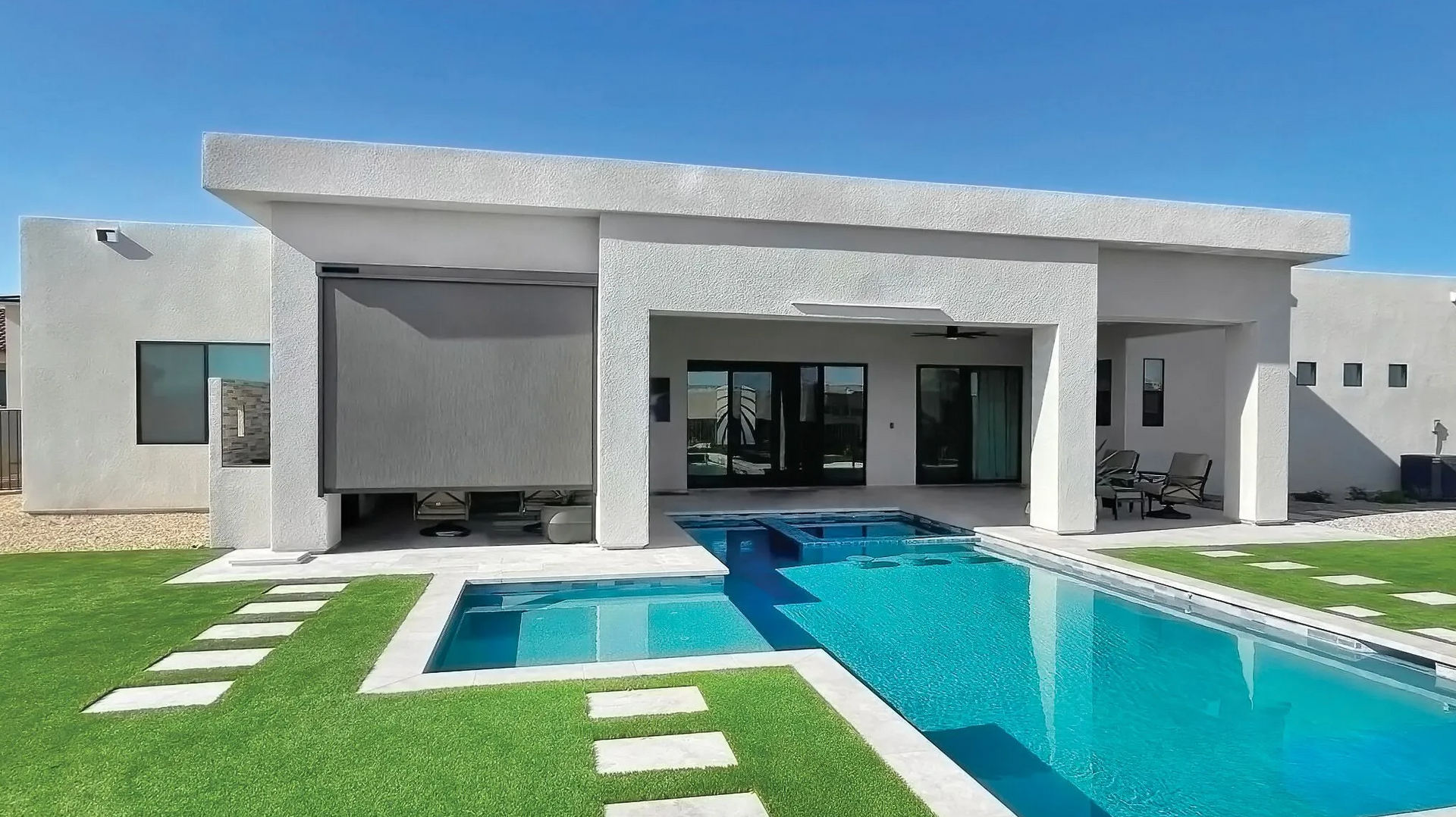 Modern white house with a turquoise pool and green lawn under a bright sky