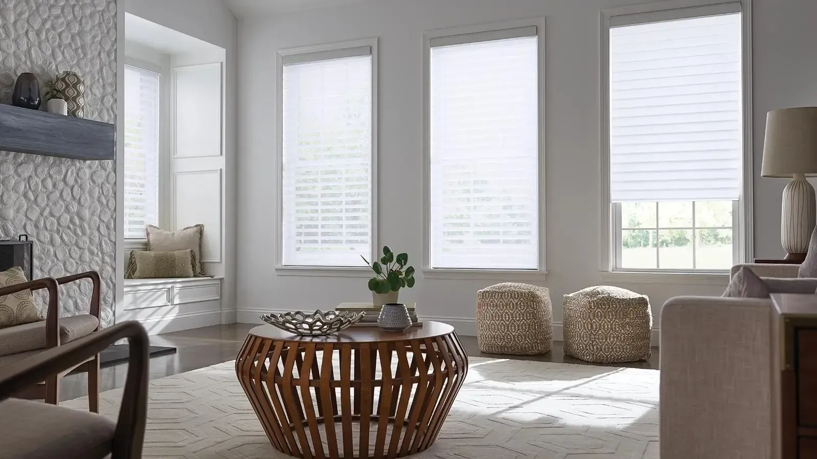 Bright living room with white blinds, wicker coffee table, and two patterned poufs by a sofa.