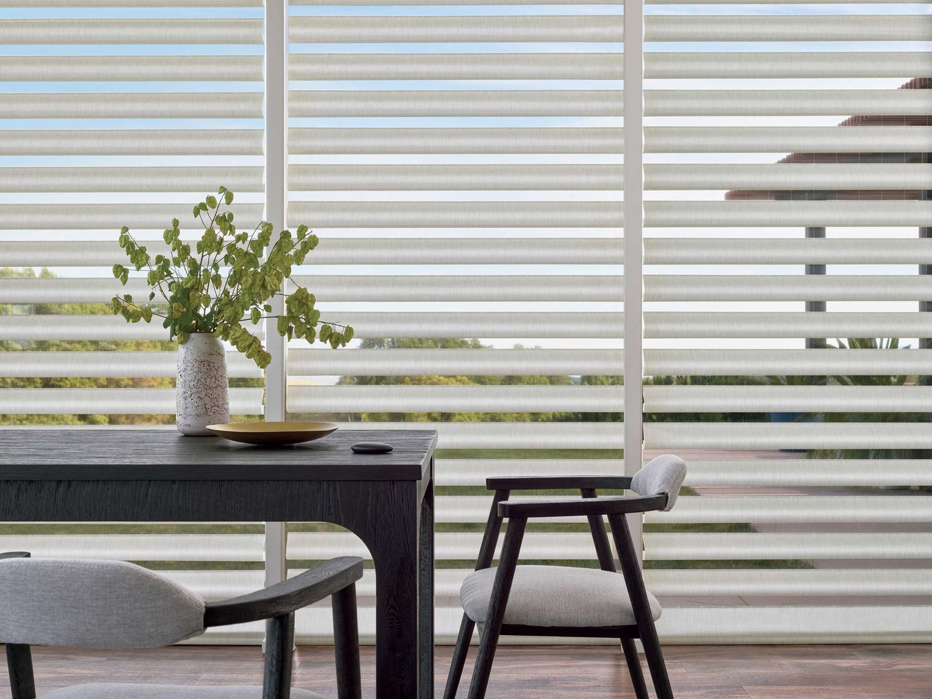 Modern interior with a round table, chair, and potted plant beside large horizontal blinds.