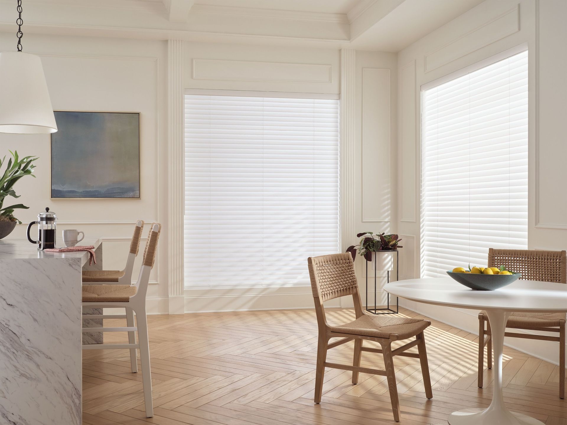 Bright dining room with wicker chairs, round table, wood floor, and tall window blinds.