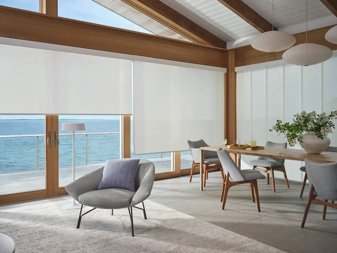 Bright seaside dining room with large windows, wooden beams, and lounge chairs facing the ocean