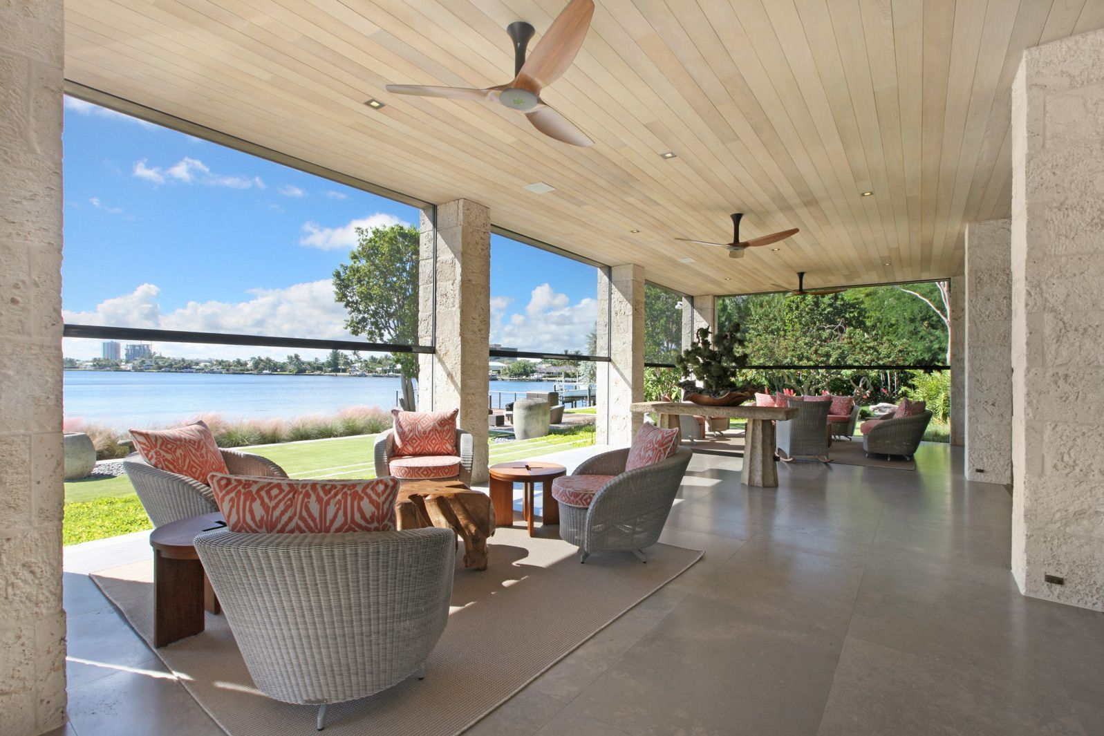 Covered lakeside patio with wicker chairs, ceiling fans, and a view of the water
