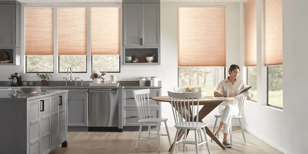 Bright modern kitchen with stainless appliances and a person sitting at a small wooden table by the window.