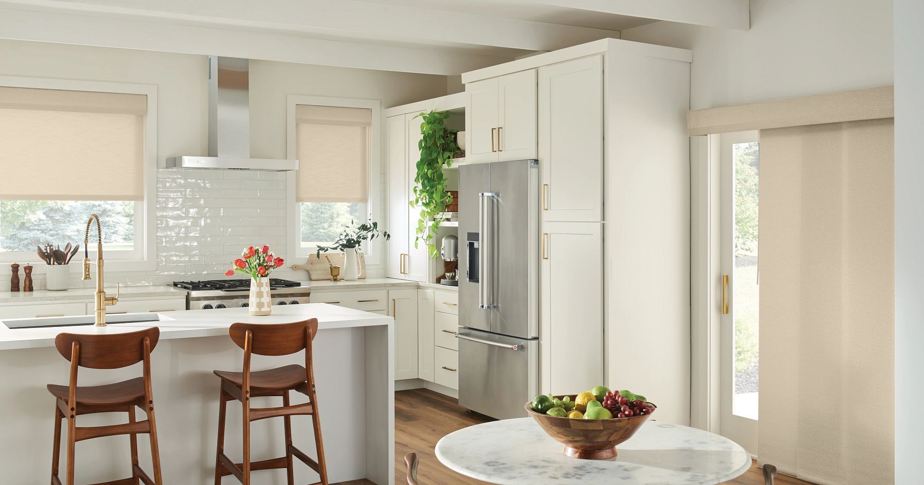 Bright modern kitchen with white island, wooden stools, and a fruit bowl on a round table