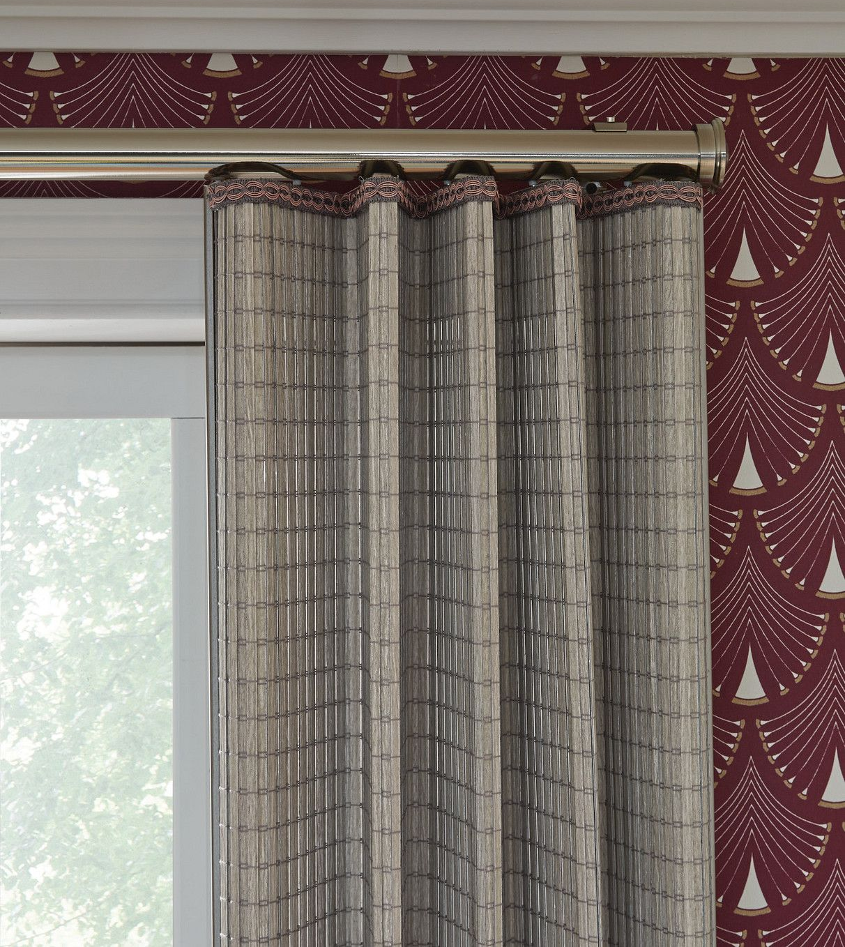 Patterned curtains framing a window in a room with burgundy wallpaper and a curtain rod, lit by daylight