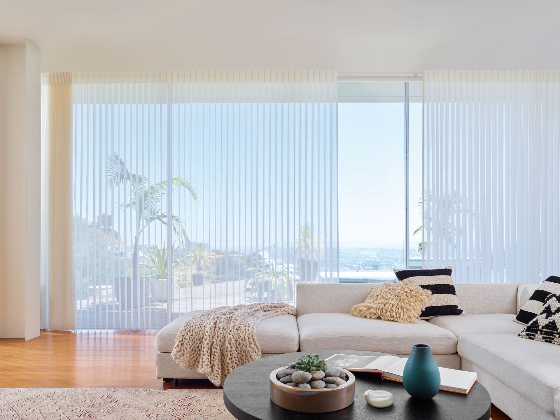 Bright living room with white sectional, wood floor, floor-to-ceiling curtains, and ocean view