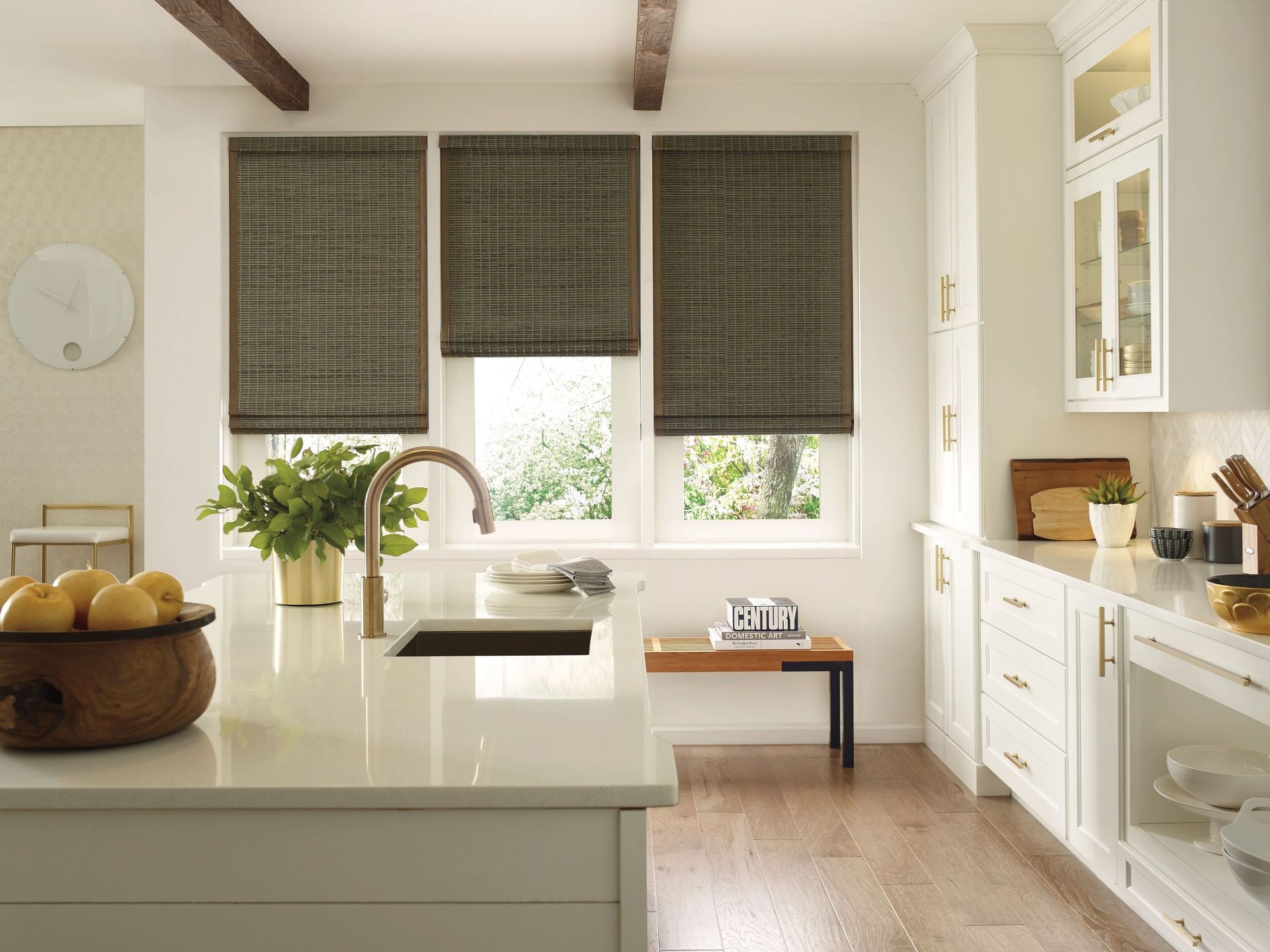 Bright kitchen with white island, farmhouse sink, patterned blinds, and fruit bowl on the counter.