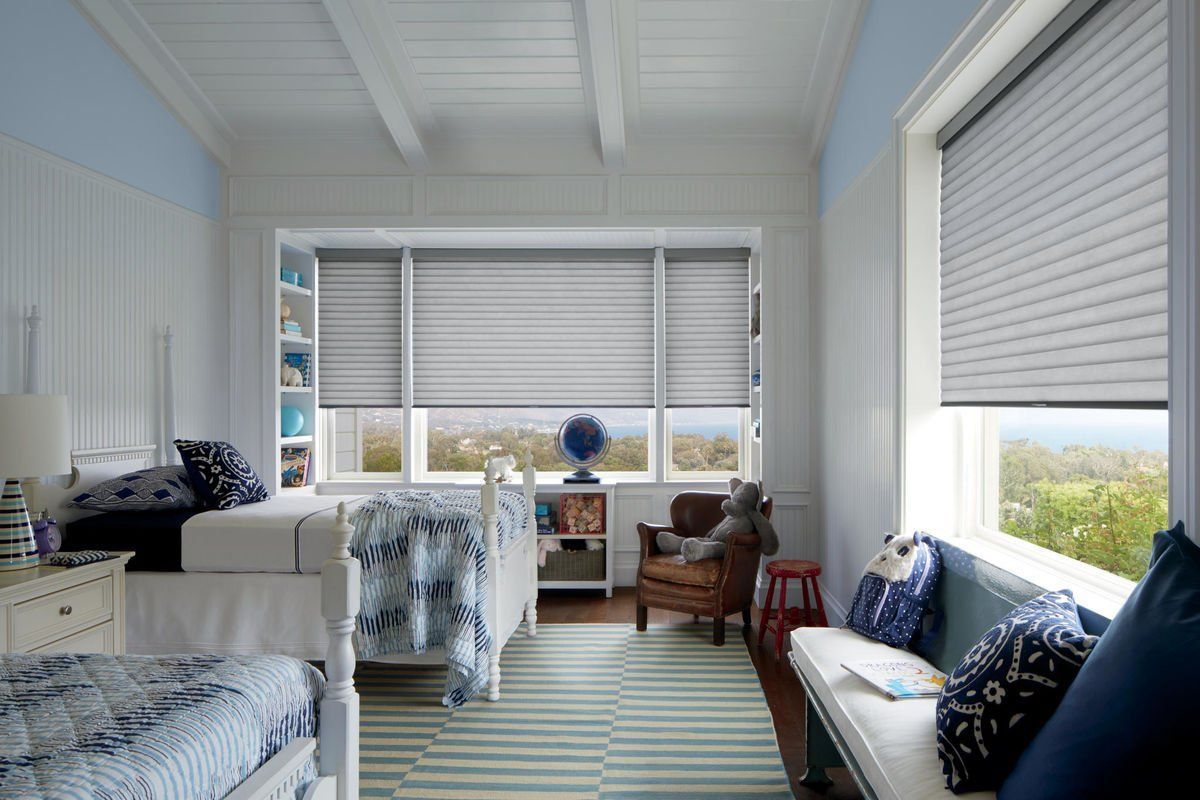 Bright sunroom with white walls, striped rug, blue cushions, and rolled shades overlooking greenery.