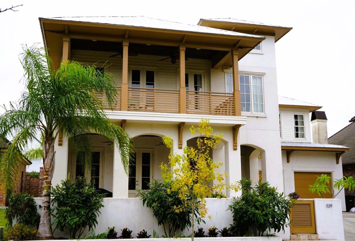 White, multi-story house with wooden balconies, and arched front porch. Palm tree in front.