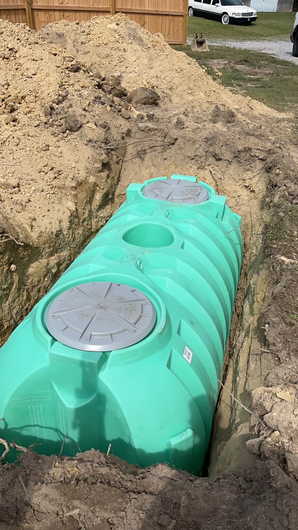 A green septic tank is sitting in the dirt next to a pile of dirt.