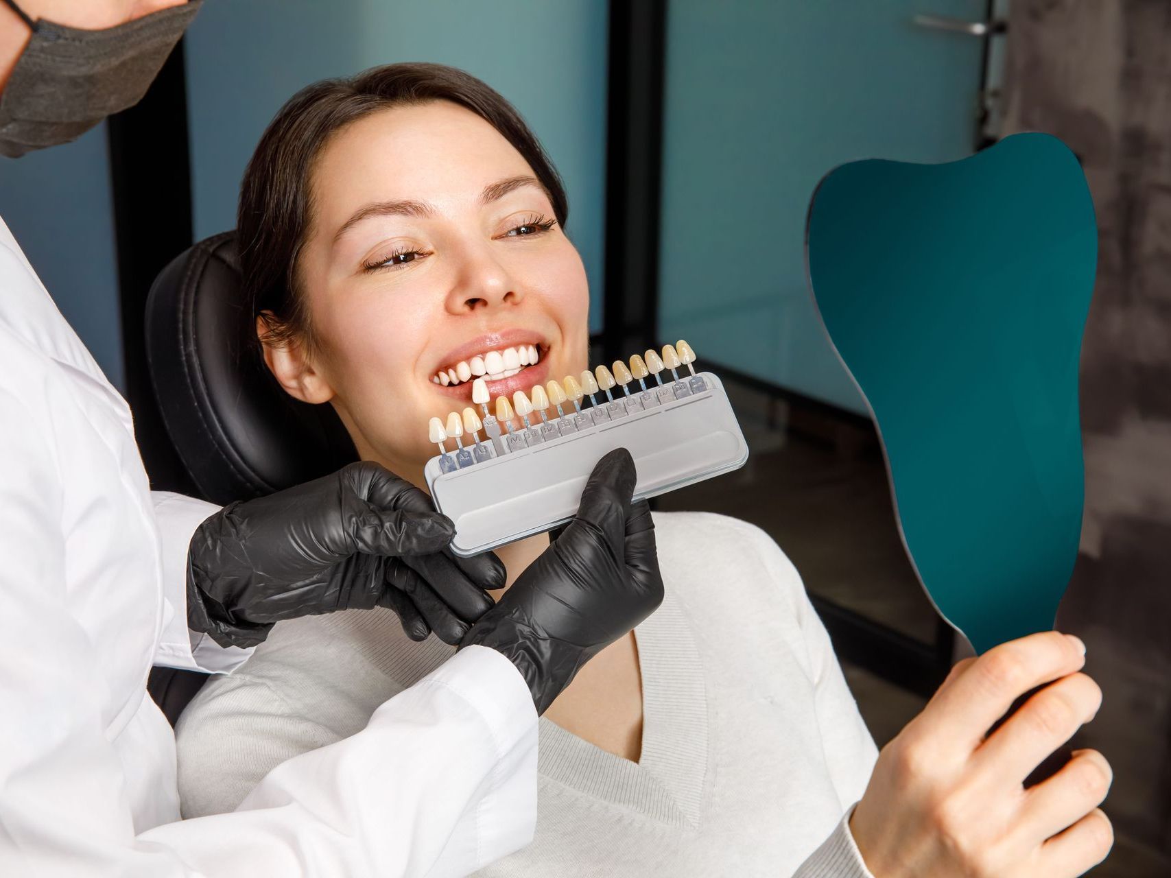 A woman is sitting in a dental chair looking at her teeth in a mirror