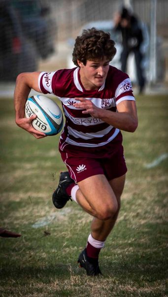 A young man is running with a rugby ball on a field.